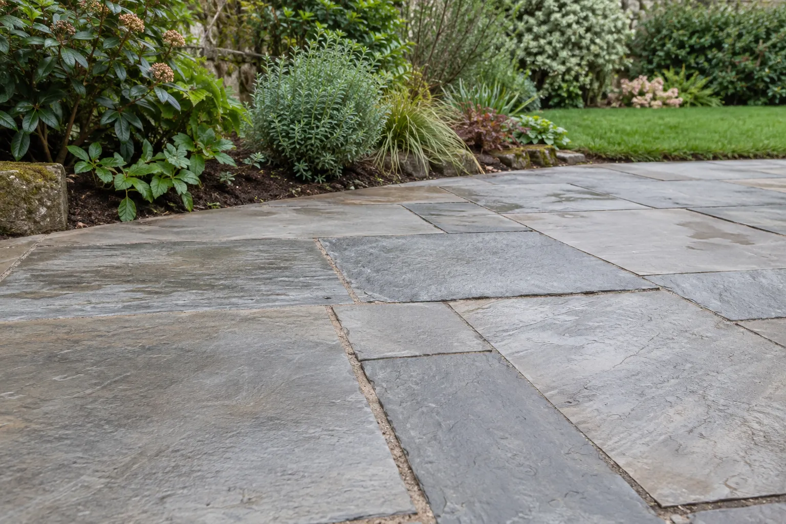 Illustrative grey stone patio beside a planted garden border